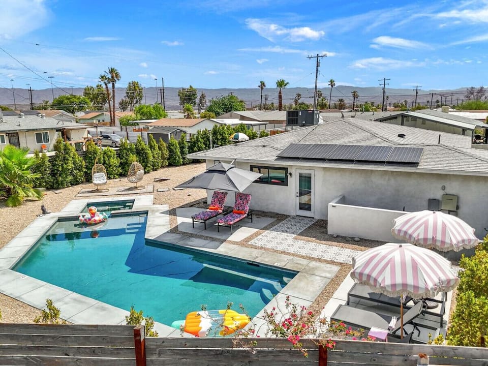 Bird’s-eye view of the backyard oasis, w/ pool, loungers & desert landscaping framed by mountain views.