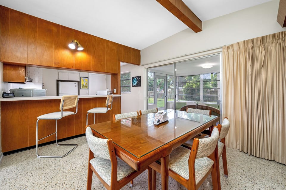 Bright and inviting mid-century dining space with wood finishes, ample natural light, and an open kitchen connection.