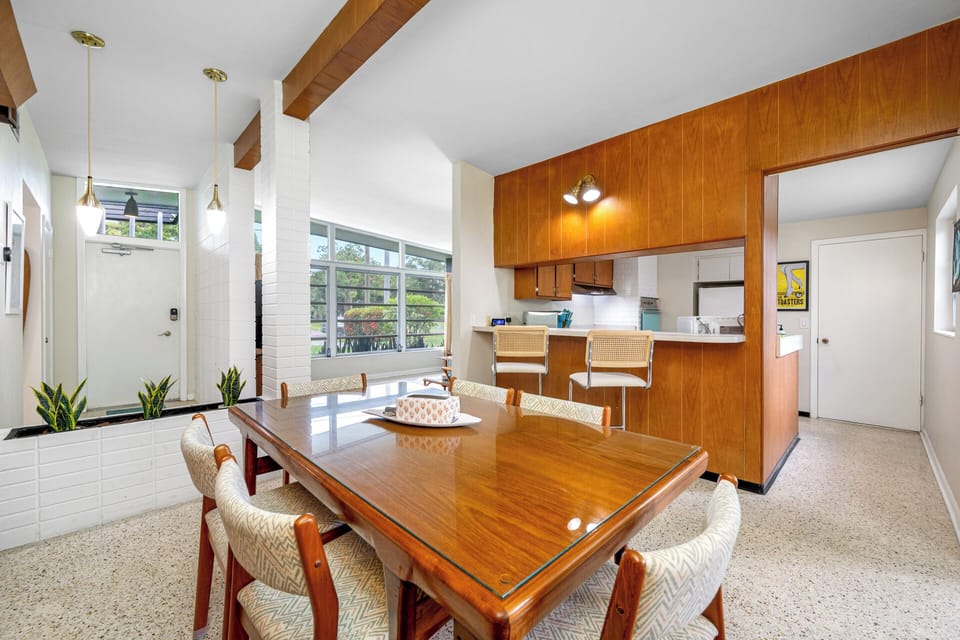 Spacious mid-century dining area with large windows, wood accents, and a connected kitchen bar.