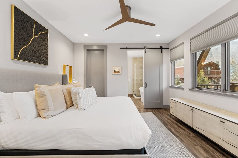 Your modern bedroom sanctuary features crisp white linens, warm wood accents, and a stylish barn door leading to your private ensuite.