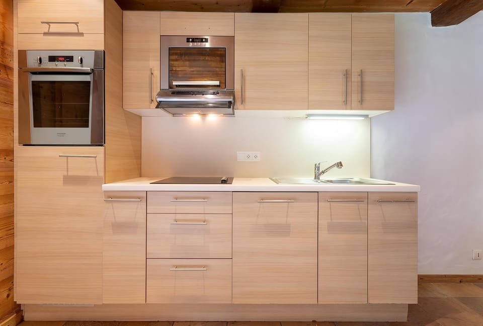 The modern kitchen features sleek wood cabinets, a built-in oven, and a microwave.  The countertops are a clean white, offering ample space for meal preparation.  The kitchen is equipped with all the necessary appliances for a comfortable stay.