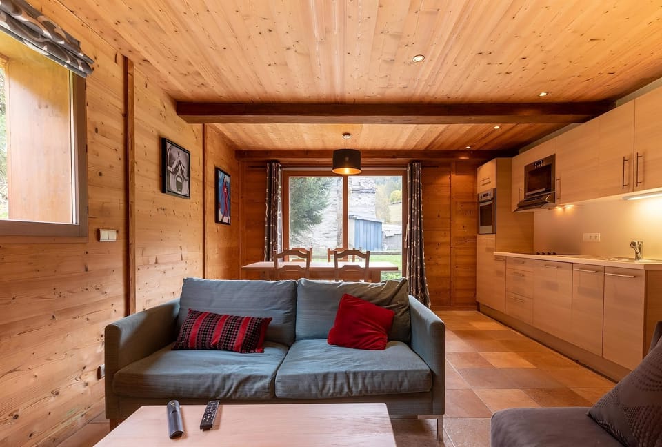 The open-plan living area is a bright and welcoming space with a comfortable sofa, a dining table, and a fully equipped kitchen.  The wood-paneled walls and ceiling create a warm and cozy atmosphere, while the large windows offer stunning views of the sur