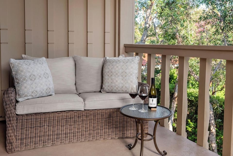 Sip wine on the cushioned balcony loveseat, surrounded by trees.