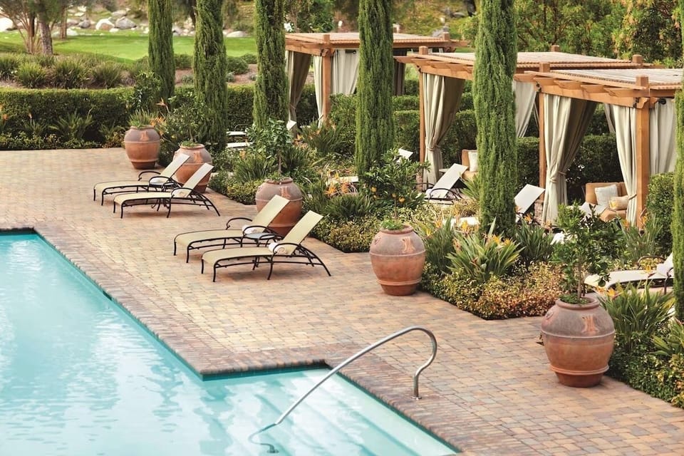 Lounge poolside in sunlit serenity beside private cabanas.