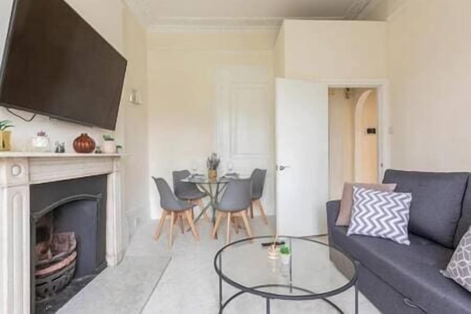 - Living room with sofa, fireplace, and dining table  
- Smart TV positioned above classic fireplace mantel  
- Comfortable setting with modern furniture and style 