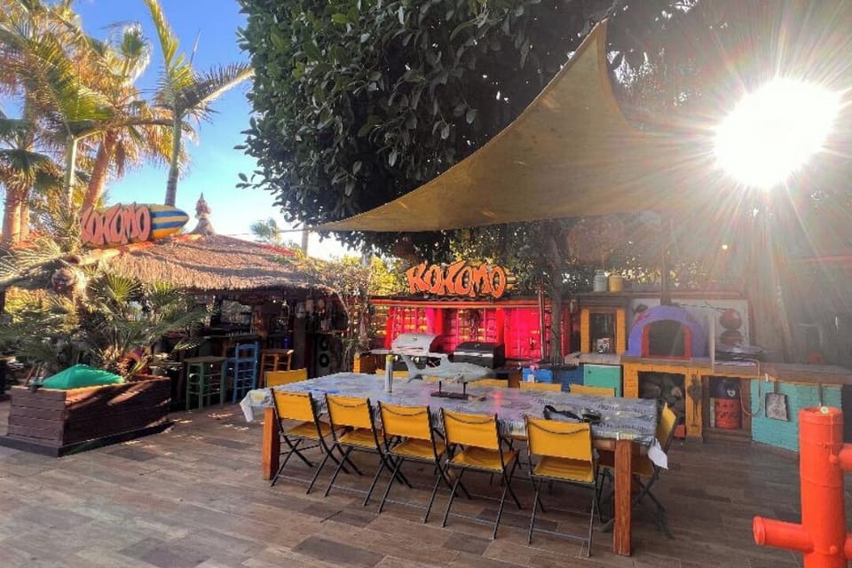 Kokomo Garden Kitchen has a Gas BBQ, a Charcoal BBQ, a fridge, a Wood-burning oven, and a Gas Paiella Cooker, and seating for 12 people under the shade of a rubber tree with overhead lighting.