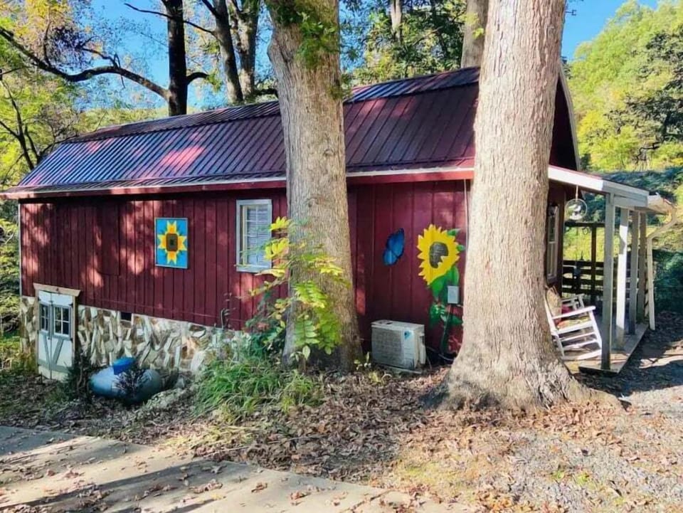 Side view of the red cabin showing colorful exterior accents, metal roof, and mature trees. Rustic mountain retreat near Bryson City attractions.