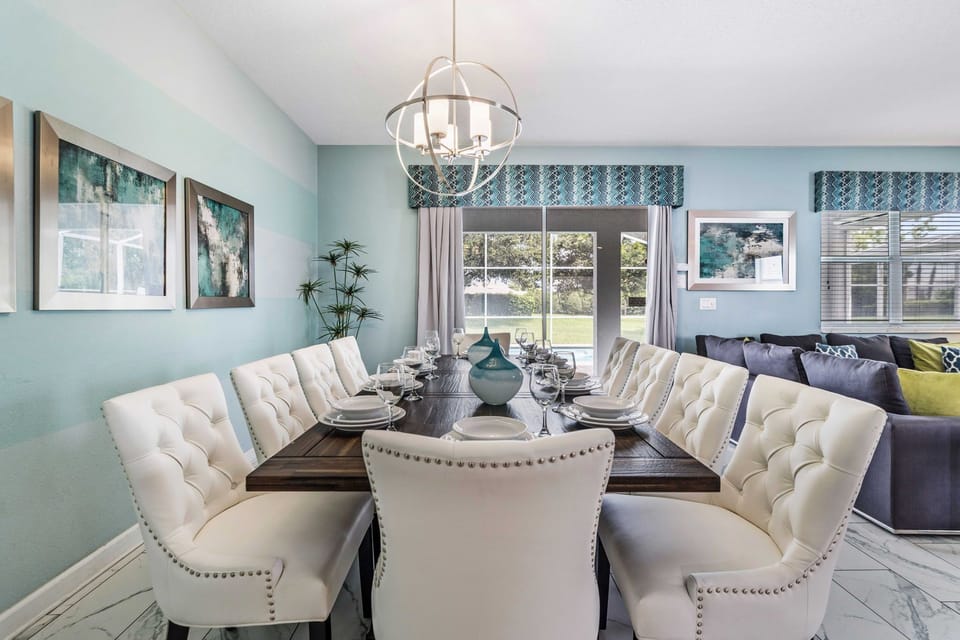 - Dining area is elegantly designed, featuring a large table surrounded by plush chairs - A stylish chandelier hangs above the table, providing a focal point - Artwork adorns the walls, while sliding glass doors lead to a well-lit backyard with pool