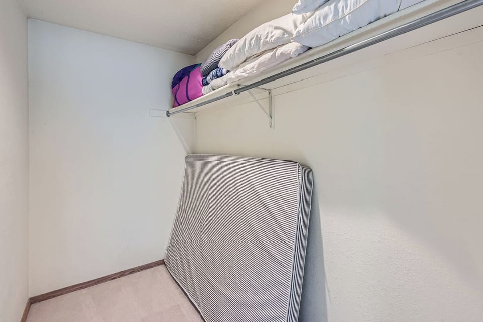 A small storage space with a folded mattress against the wall and blankets stored on a high shelf.