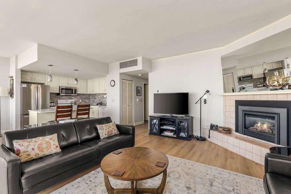 Open living and kitchen space with leather seating, cozy fireplace, TV, and bright modern finishes.