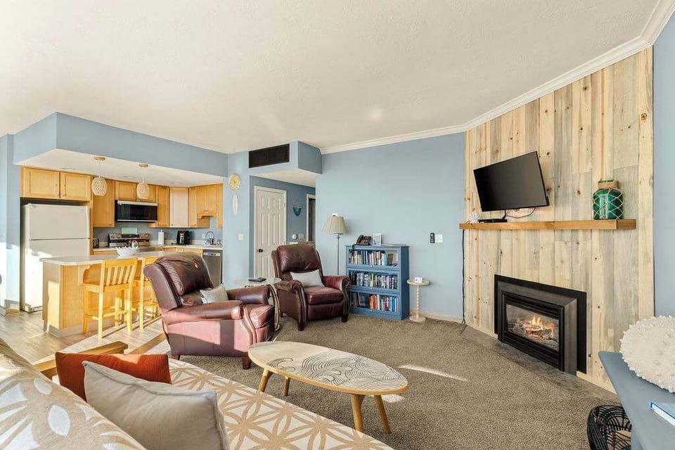Cozy open living room with fireplace, TV, and seating that flows into the kitchen and dining area.
