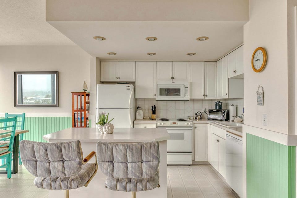 Your fully equipped coastal kitchen! Features crisp white cabinetry, essential appliances, and a convenient island with seating, perfect for preparing vacation meals.