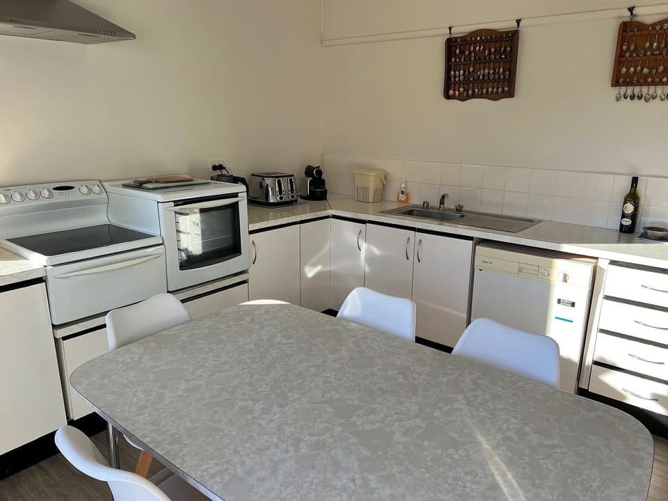 Dining table with 6 chairs, microwave, electric stove with oven, kettle, toaster, pod coffee machine, dishwasher, fridge with freezer, sliding door exiting to the side deck.