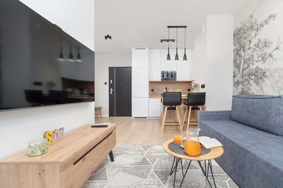 An open-plan living and dining area with a sofa and table. The space is modern with white walls and a neutral color scheme.