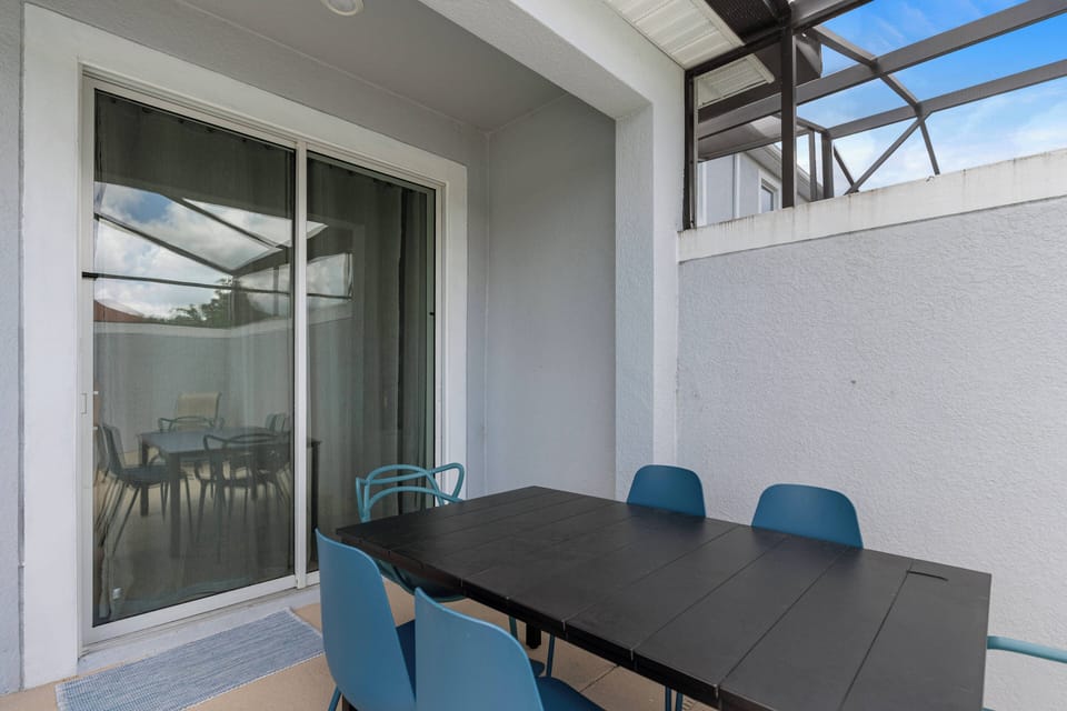 Step outside to a charming patio with a sleek black dining table and modern blue chairs, perfect for al fresco meals. Large sliding glass doors invite natural light, creating a cozy ambiance for your outdoor experience.