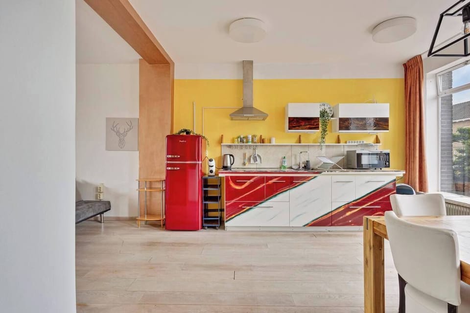 Modern kitchen with colorful cabinetry and a retro red refrigerator next to a large window.