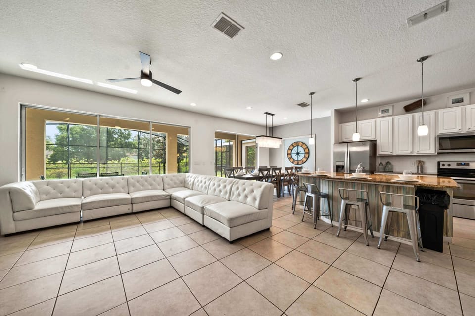 - Open-concept living room with oversized sectional and modern kitchen  
- Dining space and bar seating perfect for large family gatherings  
- Natural light and pool views make this vacation rental feel inviting