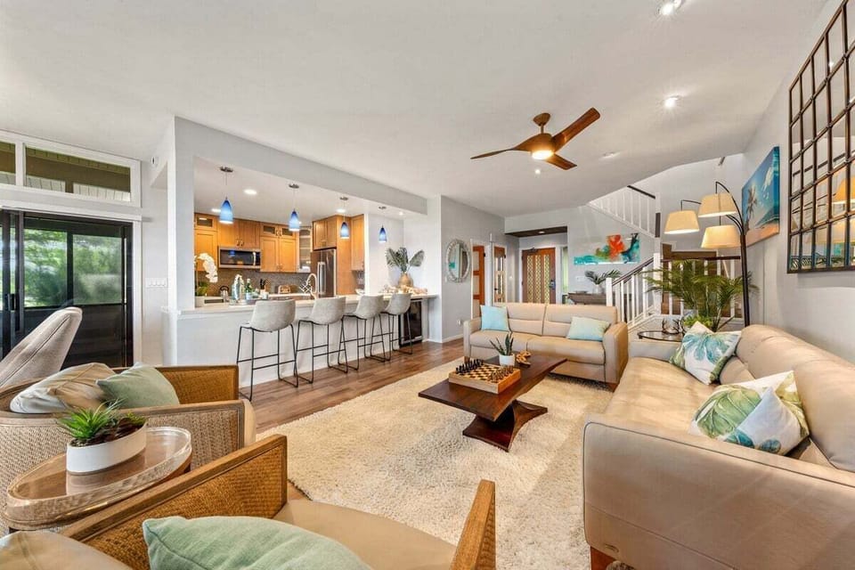 Open‑concept living area featuring coastal décor, ample seating, wood floors, and direct access to the expansive lanai.