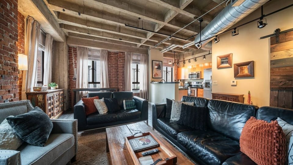 Open-concept living space with industrial charm, featuring comfortable seating, exposed brick walls, and easy access to the modern kitchen.