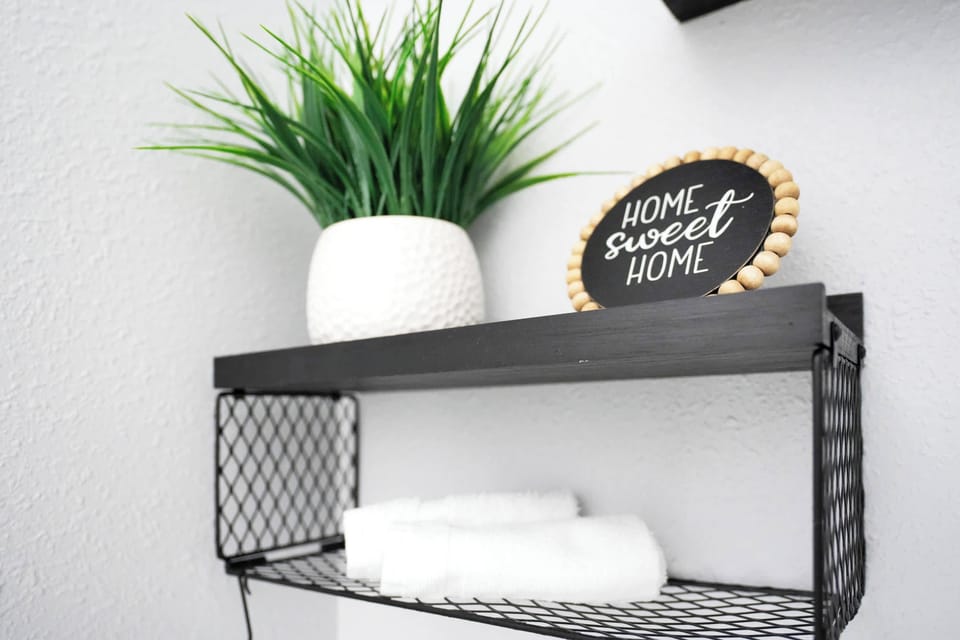 black metal shelf with white towels, a decorative plant, and a home sweet home sign