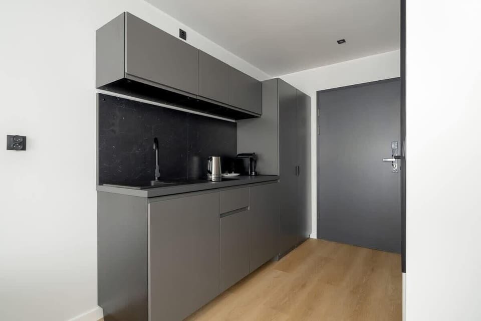 A compact kitchenette with modern appliances and cabinetry, adjacent to a hallway.