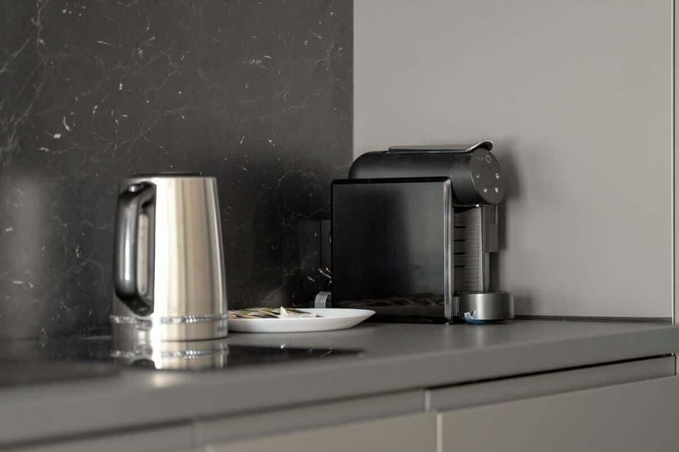 A close-up of the kitchenette countertop showing a kettle, coffee machine, and backsplash.