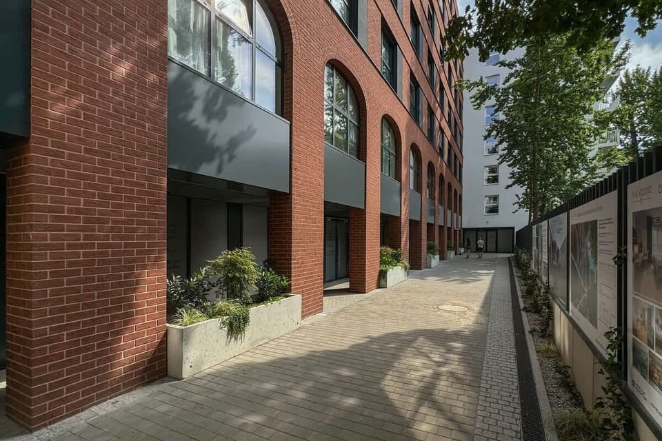 Exterior view of the building’s entrance path, showing brick walls and plants.
