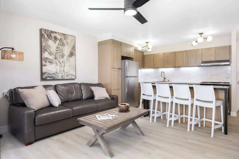 The modern living area is seamlessly connected to a beautifully appointed kitchen, featuring a comfortable sofa and a breakfast bar with 4 sleek white stools, perfect for socializing and light meals!