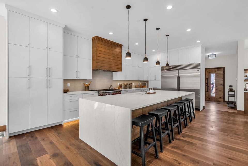 Kitchen counter, dozens of shelves, black chairs and luxury fridge.