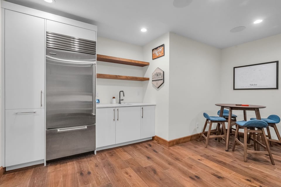 Fridge in the game room at Woodside Main Street Haven, along with a sink and other furnishings.