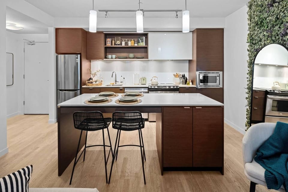 A contemporary kitchen space featuring a large central island with a wood-accent breakfast bar and minimalist barstools.