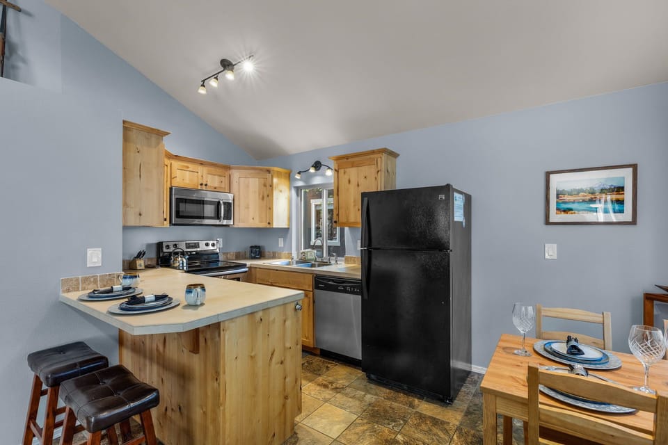 Your bright, welcoming kitchen features natural wood cabinetry, modern appliances, and a cozy breakfast bar with dining space—perfectly equipped for preparing meals and gathering during your stay.