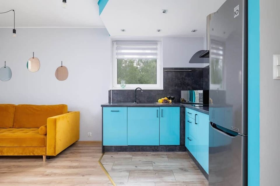 In this cheerful living room, a vibrant yellow sofa and turquoise kitchen cabinets make the space feel fresh and energetic.