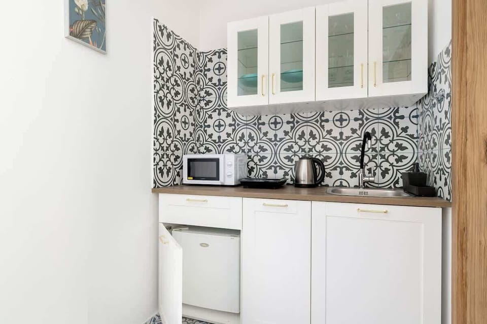 Compact kitchenette with patterned backsplash, white cabinets, and essential appliances for simple meals.
