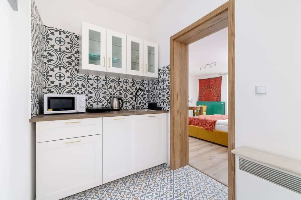 Compact kitchenette with patterned backsplash, white cabinets, and essential appliances for simple meals.