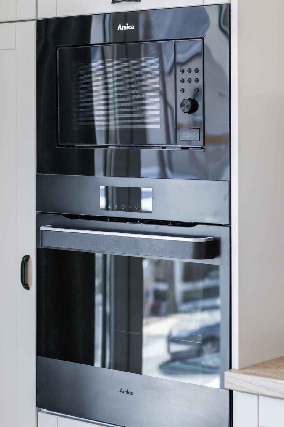 The image showcases a built-in oven and microwave, seamlessly integrated into tall white cabinetry reflecting the minimalist design, making the kitchen both functional and stylish.