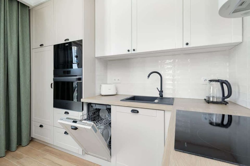 The kitchen features a clean, modern design with white cabinets, a marble-style countertop, and a black faucet paired with a matching black sink, creating a sleek contrast, while natural light from the nearby windows enhances the open and airy feel o