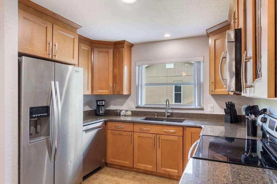{KITCHEN} The open kitchen, seamlessly connecting to the living and dining areas, includes a spacious island, French door fridge, stove/oven, dishwasher, coffee maker, and all the essentials for cooking and enjoying meals.