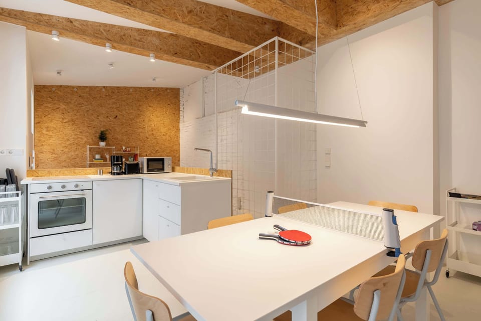 A fully equipped white kitchen meeting a bright dining space — functional, spacious and ideal for shared meals or work sessions.