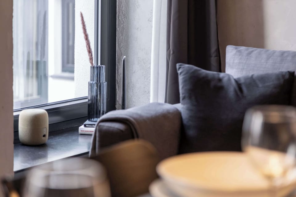 A decorative close-up by the window, featuring a textured vase, a sculptural side object, and soft fabrics. Subtle styling complements the apartment’s modern concrete aesthetic.