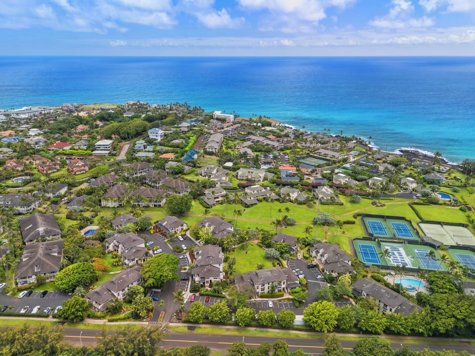 Stunning aerial view of the resort community nestled along the pristine Hawaiian coastline, showcasing lush tropical grounds, tennis courts, and direct beach access within a peaceful oceanfront neighborhood.