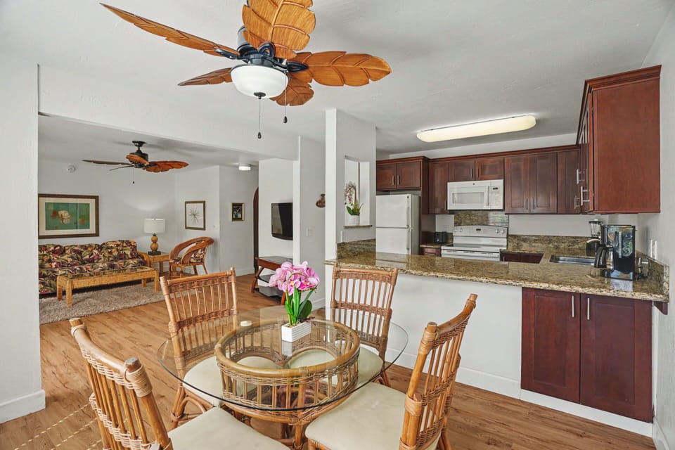 You'll love the open-concept flow connecting your dining area to the living space and kitchen, with tropical-style ceiling fans and warm wood accents creating an inviting island atmosphere.