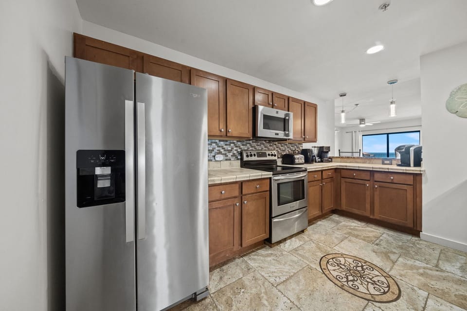 Your fully equipped kitchen features stainless steel appliances, warm wood cabinetry, and gleaming tile floors—perfect for whipping up meals while soaking in views through bright windows.