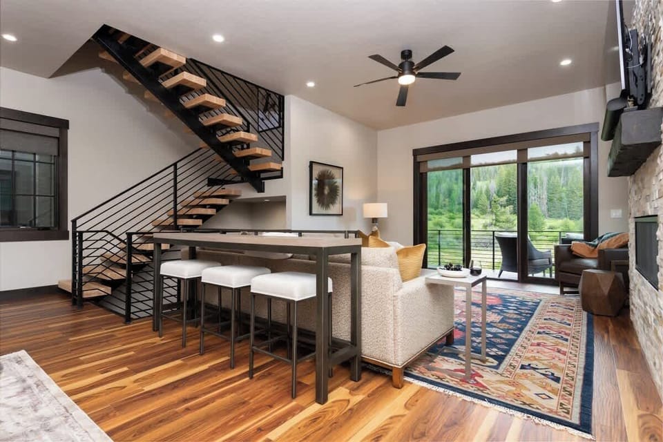 - Unwind in this open concept living space featuring floating stairs and tall ceilings
- Bar seating, fireplace views, and forest light complete the vibe
- Ideal for group stays with space to relax, dine, and reconnect