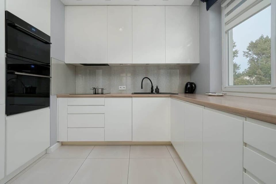 White modern kitchen with light flooring and black sink.