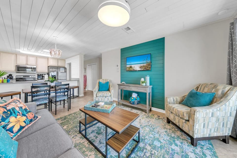 Relax in your bright, coastal-themed living space with turquoise accents and open kitchen—perfect for memorable vacation moments.