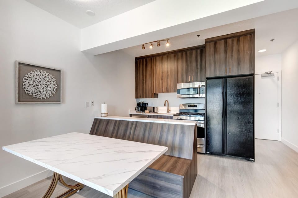    Stylish kitchenette with marble-top dining, wood bench, and modern appliances.