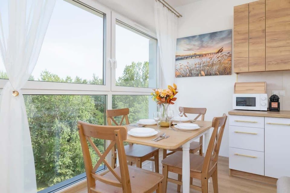 Intimate dining space next to a large window, allowing natural light to flood in, with a wooden dining set and fresh flowers on the table.