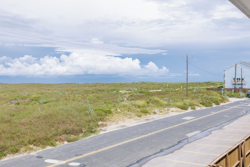 Coastal road winds through natural dunes and grasses, with utility lines and beach access nearby.