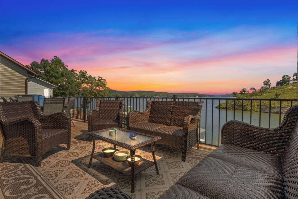 Enjoy breathtaking sunset views from this serene lakefront deck, featuring cozy wicker seating and a warm ambiance perfect for a peaceful evening escape.